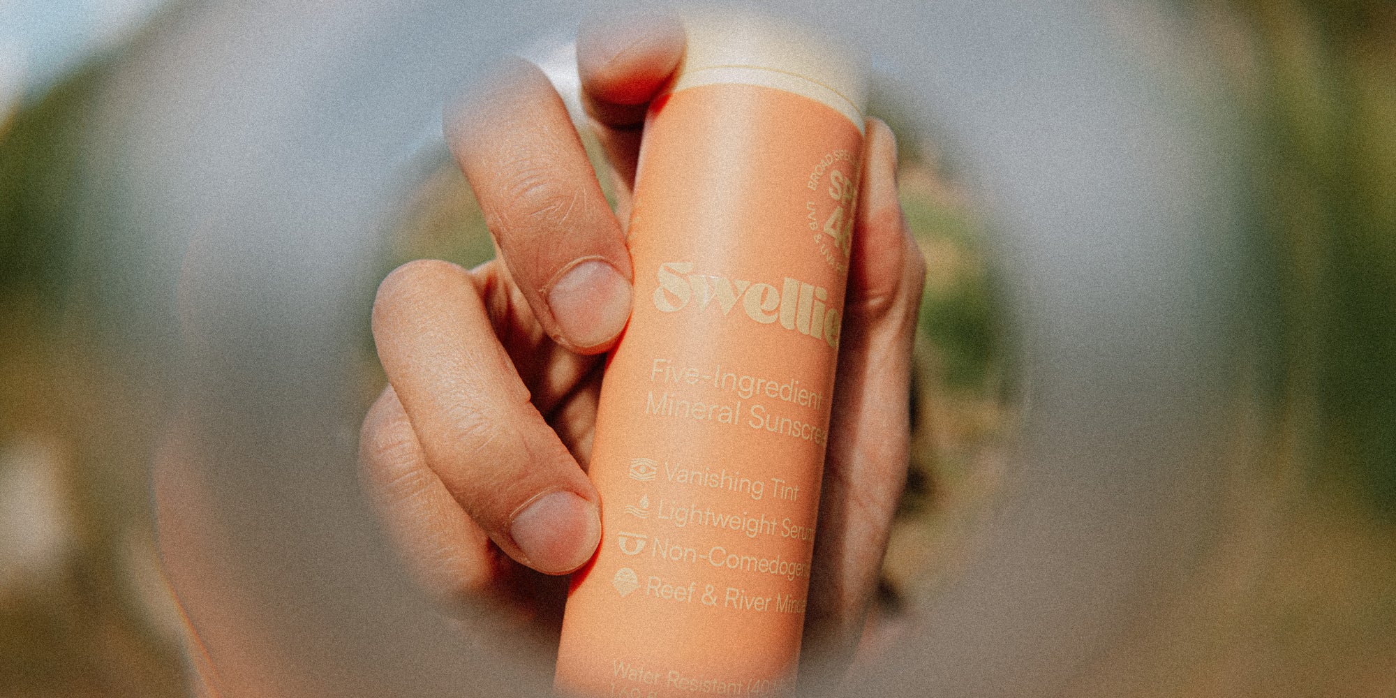 A person holding a bottle of Swellies five-ingredient mineral sunscreen outdoors in the sun
